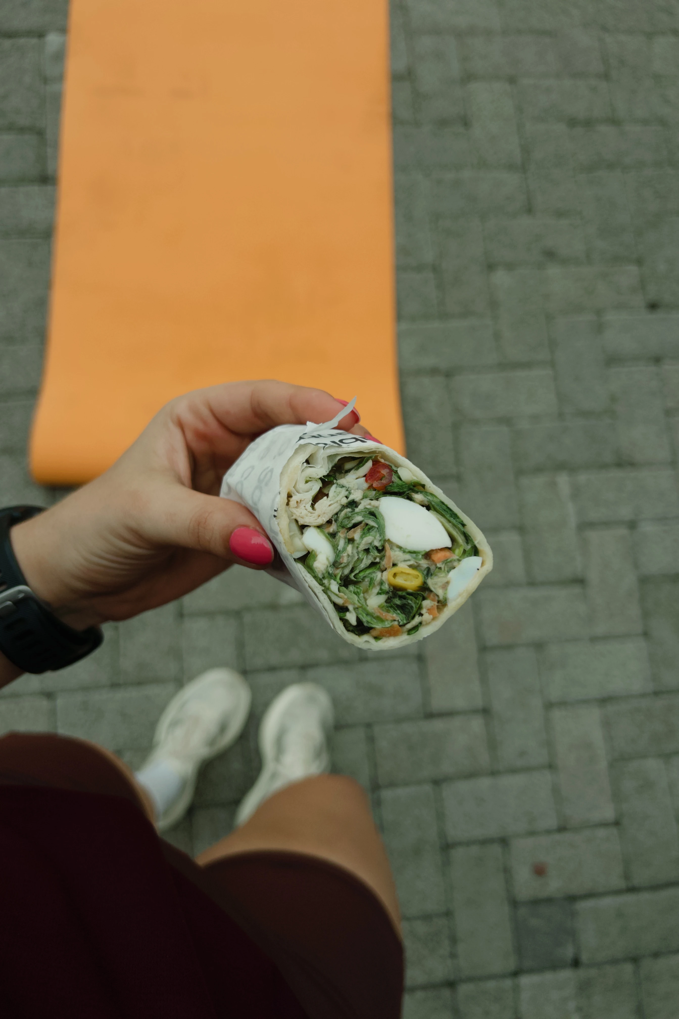 Mãos segurando um wrap artesanal fresco e farto com vegetais crocantes e proteína magra.