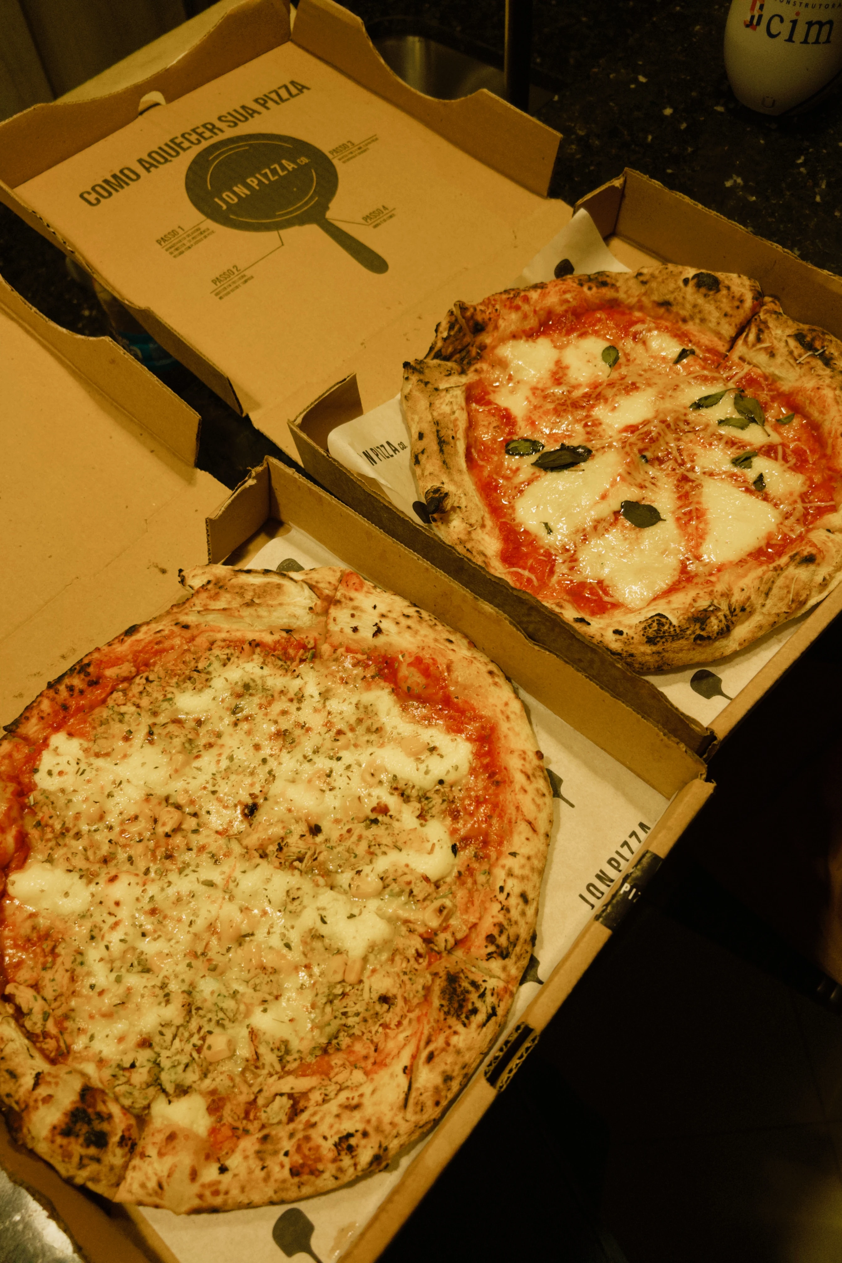 Duas caixas abertas de pizza artesanal de fermentação lenta com queijo derretido e folhas de manjericão da Jon Pizza Co.